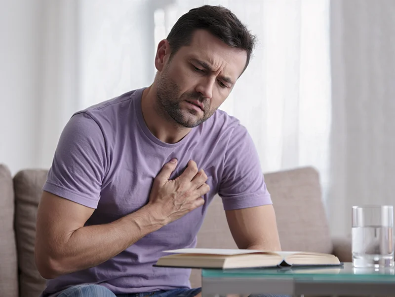 Мужчина держит руку на груди от боли